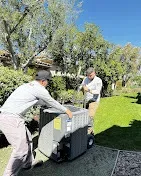 Two workers installing an outdoor air conditioning unit in a sunny garden.